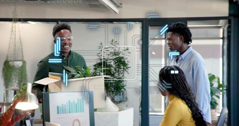 Carrying moving box with plants into modern open-plan office, colleagues welcoming and smiling