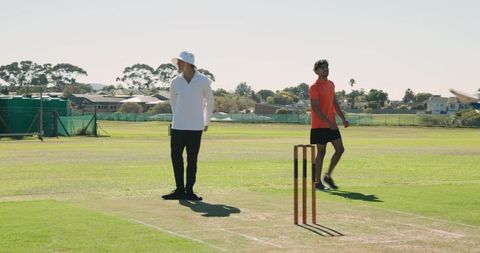 Indian bowler starting run-up on sunlit cricket pitch with umpire and batsman