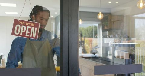 African american barista welcoming customers at coffee shop entrance with open sign