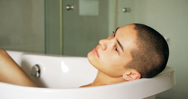 Person with a shaved head lies in a bathtub, embodying serenity and calmness. This can be used to illustrate themes of self-care, relaxation, mindfulness, and tranquility. Ideal for wellness and lifestyle content promoting the importance of taking time for oneself.
