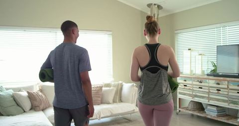 Couple carrying yoga mats preparing home workout in bright living room casual activewear wellness