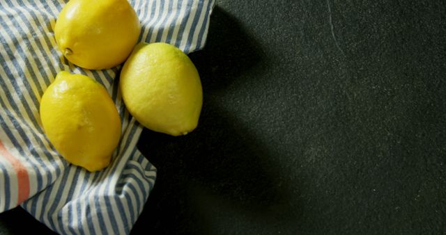 Bright yellow lemons rest on a striped cloth against a dark background, with copy space - Download Free Stock Photos Pikwizard.com