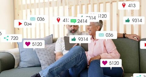 Laughing mature couple sharing tablet on cozy sofa with social media notification overlays