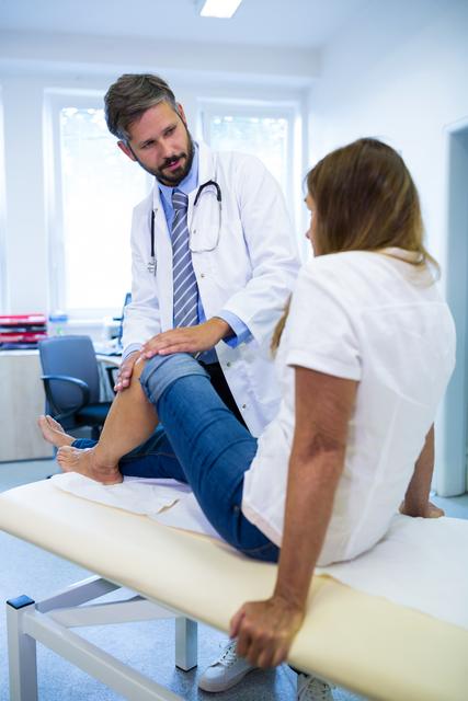 Male doctor examining patient's knee in a hospital setting. Ideal for medical websites, healthcare brochures, and articles about knee injuries, medical consultations, and patient care.