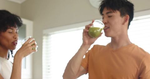 Multiracial couple drinking green smoothies in bright home kitchen morning routine