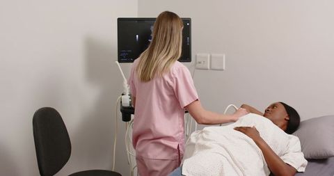 Female clinician performing abdominal ultrasound on black patient in clinic room