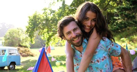 A joyful couple is spending time together at a summer festival, surrounded by a vibrant outdoor environment. The setting is cheerful and relaxed, making it a suitable image for advertising events or products related to festivals, camping equipment, lifestyle solutions, or romantic getaways. The photo can also be used for blogs and articles highlighting summer fun or couple's adventures.