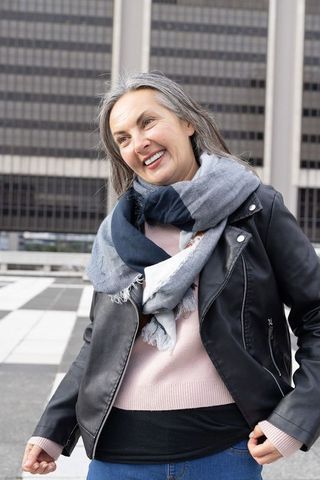 Smiling senior woman enjoying city stroll in leather jacket and gray-blue scarf