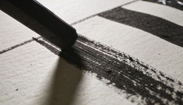 Charcoal stick creating bold textured stroke on paper close-up macro art markmaking