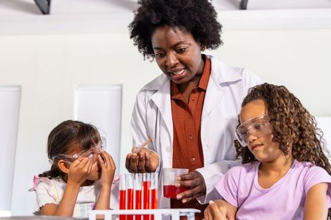 Teacher guiding kids through hands-on science experiment with safety goggles and beakers