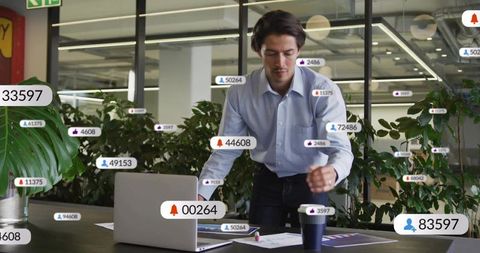 Mid-adult professional scanning laptop amid floating notifications in biophilic office