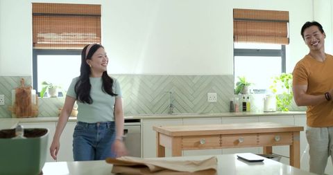 Asian couple enjoying morning in modern bright kitchen with wooden island and plants