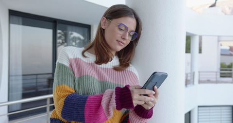 Woman Relaxing on Balcony Checking Smartphone in Colorful Sweater