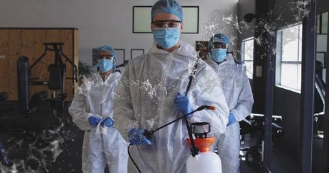 Sanitation team disinfecting gym in full PPE using handheld sprayer and coveralls