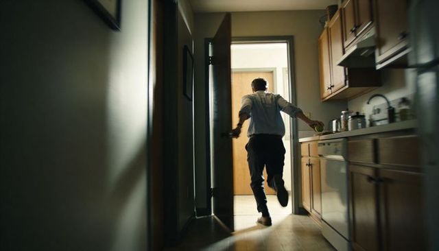 Hurrying man running from kitchen carrying apple toward bright doorway in motion