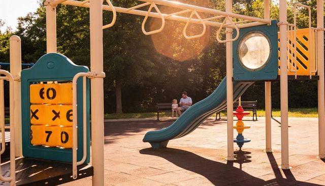 Father and toddler sitting on bench near playground slide during golden hour
