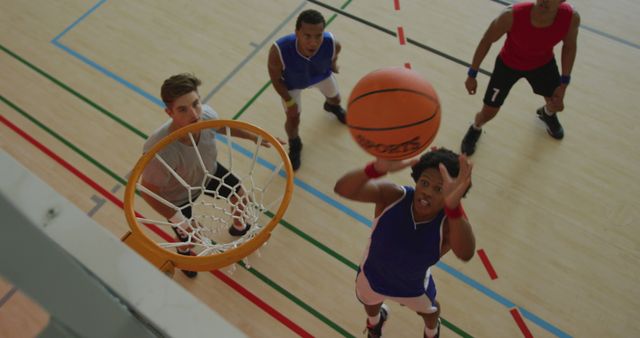 Overhead view of african american male basketball player scoring goal against diverse players. basketball, sports training at an indoor court.