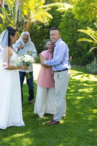 Intergenerational diverse family celebrating backyard wedding hugging under sunlight