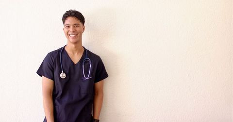 Smiling male nurse in scrubs with stethoscope against plain background