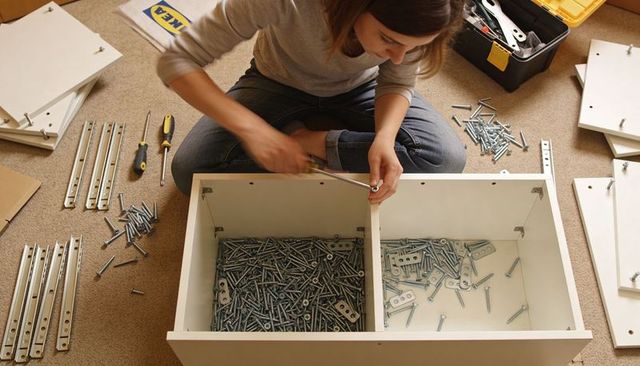 Woman assembling flatpack white cabinet on carpet fastening divider with screwdriver