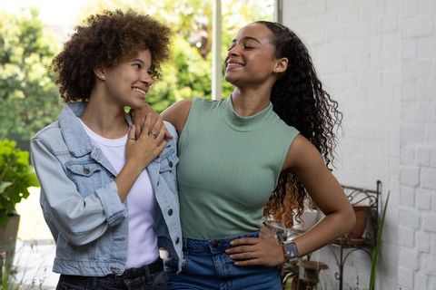 Smiling friends sharing warm moment on sunlit porch, casual denim and greenery