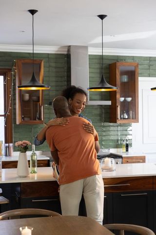 African american couple hugging at modern kitchen island with green backsplash and wine