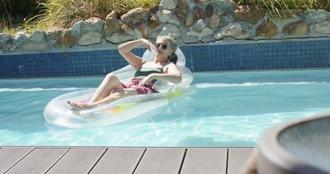 Mature asian woman relaxing on inflatable lounger in backyard pool on sunny day