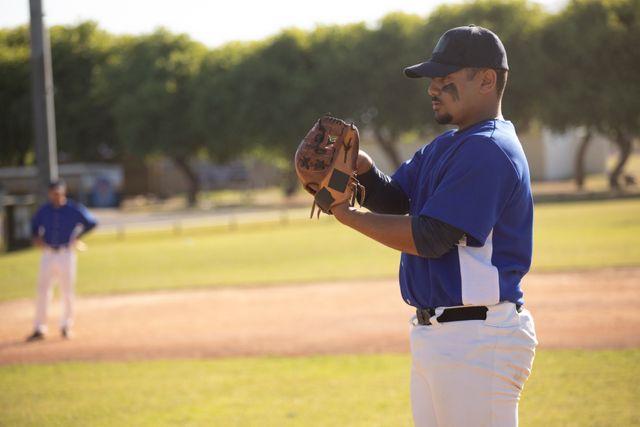 Biracial male baseball pitcher standing on the mound, preparing to throw the ball during a game on a sunny day. Ideal for use in sports-related content, articles about baseball, athletic training materials, or promotional materials for baseball events.