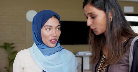 Indian women colleagues discussing project in modern office wearing hijab and tunic