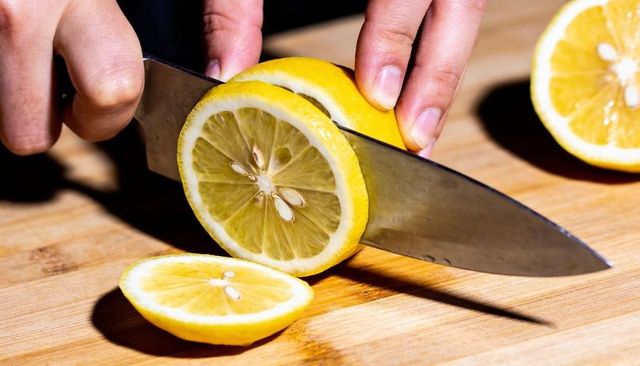 Slicing lemon with chef knife on wooden board close-up showing seeds and dramatic shadow
