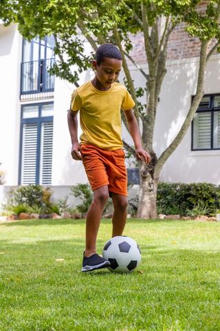 African american boy practicing soccer drills on sunny suburban lawn
