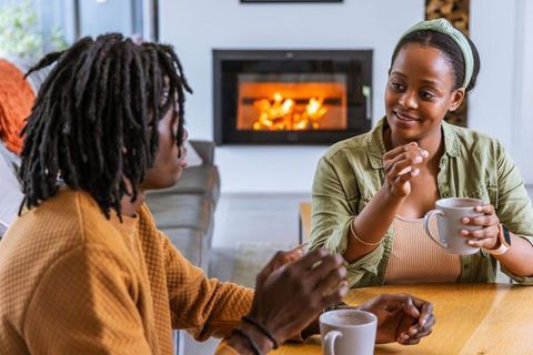 African american couple sharing warm coffee conversation by fireplace in cozy living room