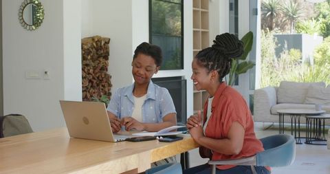 African american mother and daughter studying together at home using laptop and notebooks