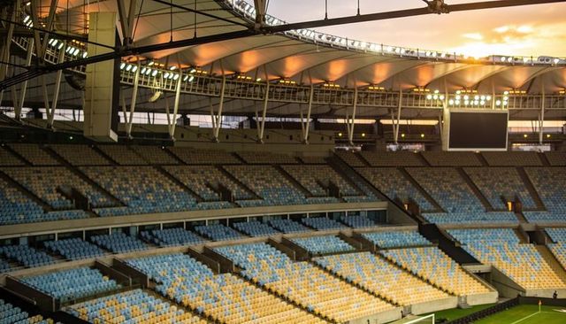 Empty stadium seats glowing at sunset under curved canopy with scoreboard