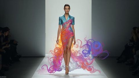 Striding model wearing teal bodice with swirling vibrant trailing skirt on couture catwalk