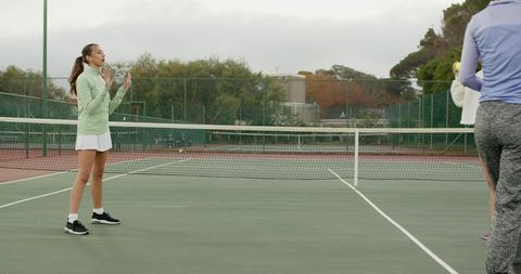Female tennis teammates communicating at net during coaching session on outdoor court