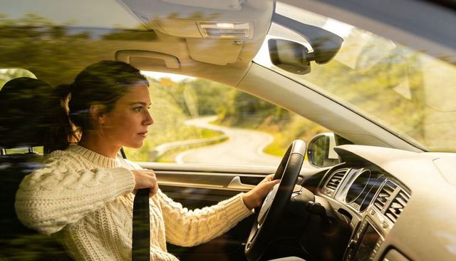 Woman fastening seatbelt while driving on winding country road through sunlight