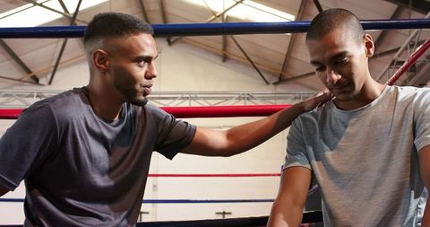 Sparring partner comforting fatigued boxer in ring corner during training