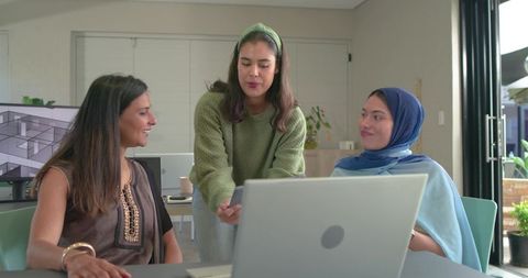 Diverse female team collaborating around laptop in modern design studio workspace