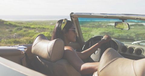 Indian woman driving convertible along sunlit coastal road enjoying seaside roadtrip