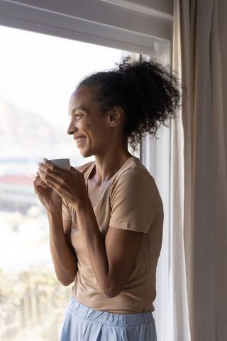 African american woman enjoying morning coffee by window, smiling in soft natural light