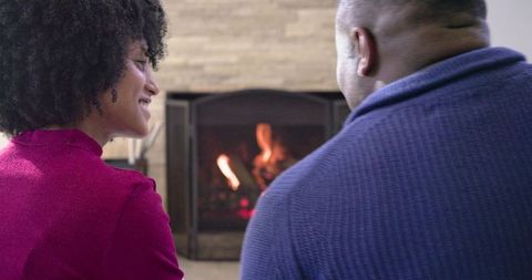 Couple enjoying cozy fireplace conversation wearing sweaters in home living room