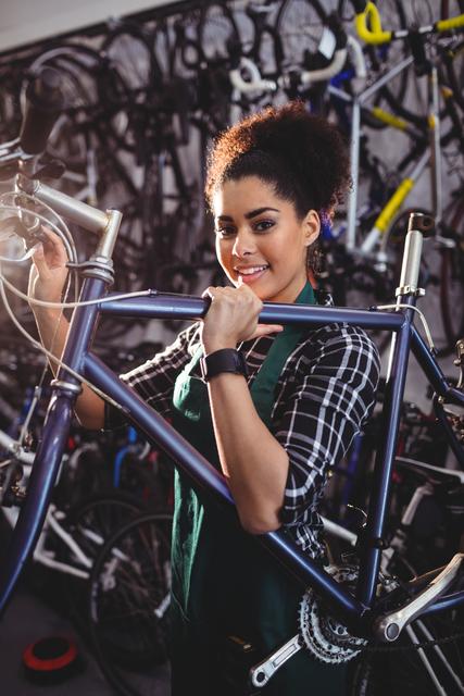 Female mechanic holding bicycle in workshop, smiling confidently. Ideal for use in articles or advertisements related to bicycle repair services, professional mechanics, or cycling enthusiasts. Can also be used for promoting workshops, bike maintenance tutorials, and repair shop services.