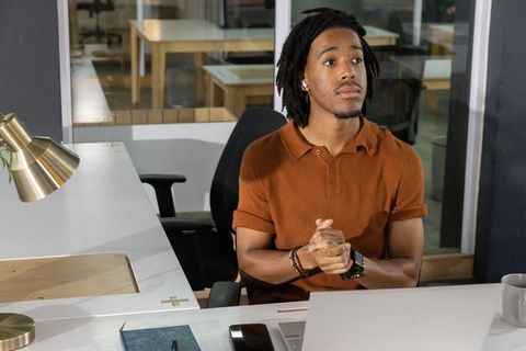 African american man working at laptop in modern coworking space wearing rust-brown polo