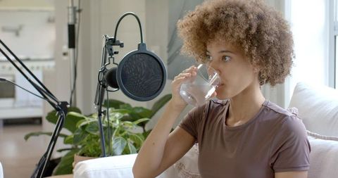 Podcaster drinking water while recording at home with microphone and natural light