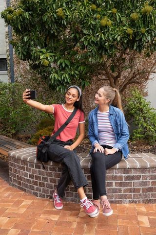 Two young women taking selfie on outdoor brick bench casual friendship lifestyle vibrant