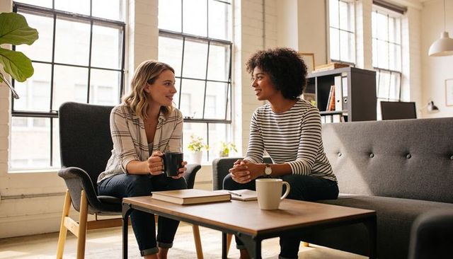 Two colleagues chatting over coffee in sunlit coworking lounge for casual collaboration