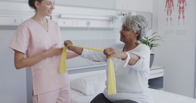 Elderly woman performing exercises with resistance band guided by physical therapist in a healthcare setting. Suitable for topics related to physical therapy, rehabilitation, aging, senior health, and healthcare services.