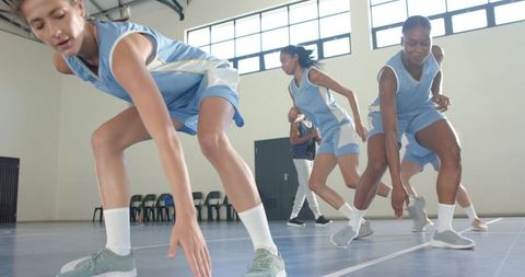 Focused female basketball team practicing defensive drills indoors