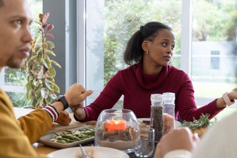 Black woman gesturing during tense dinner conversation while holding partner's hand